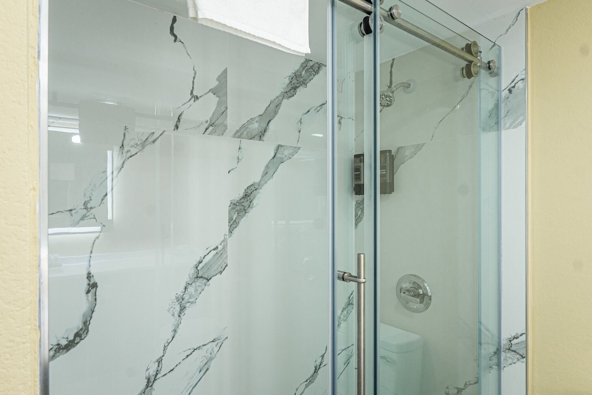 A glass-enclosed shower with a marble-like wall design.