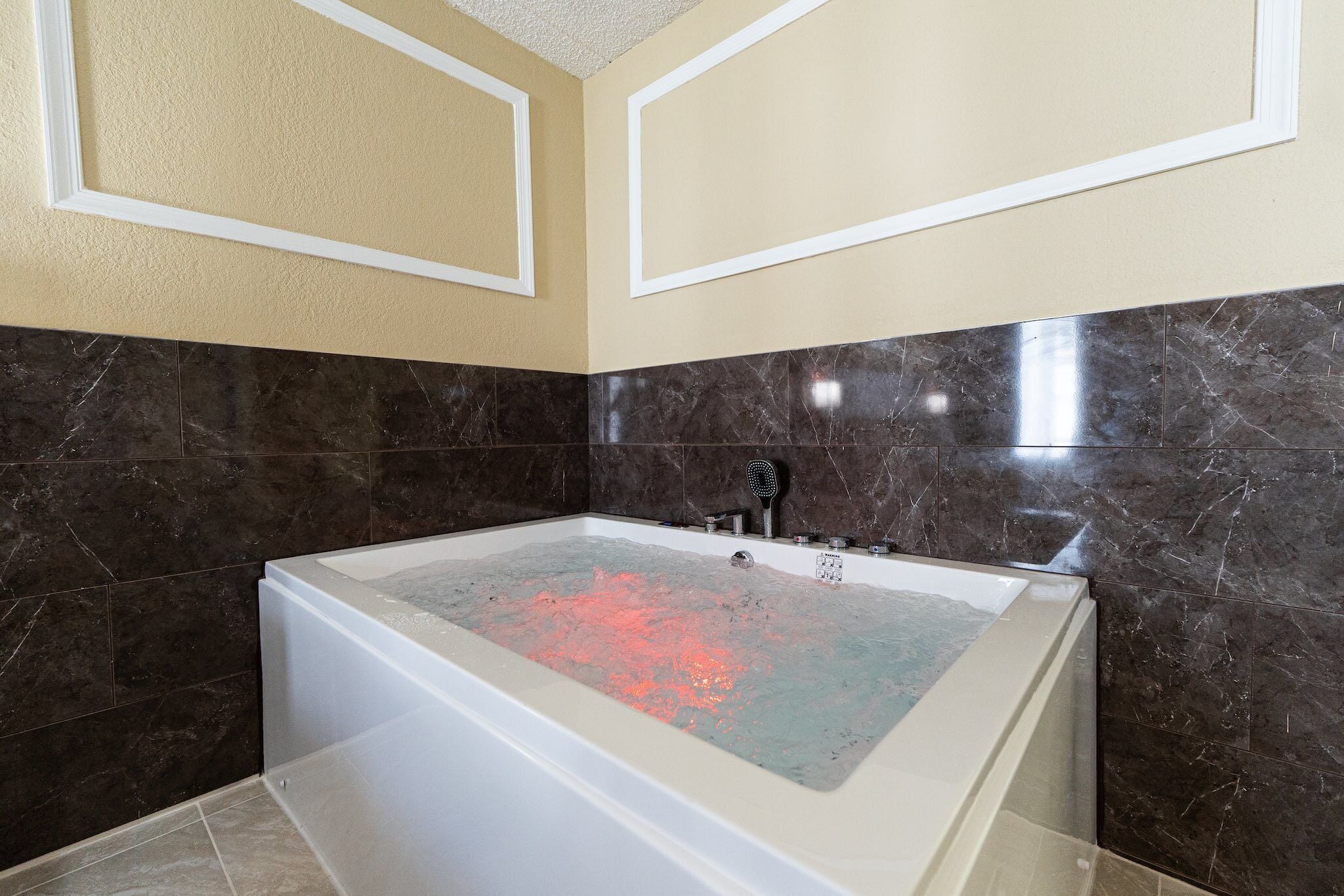 Un baño con una bañera grande, paredes de mármol oscuro y techo color beige.