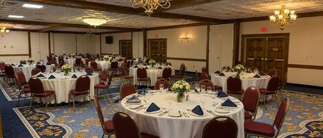 A banquet hall with round tables, red chairs, and a blue carpet with gold patterns.