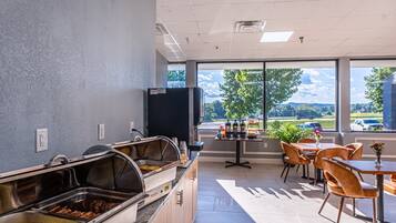 A buffet area with various food stations, a seating area with tables and chairs, and a view of the outdoors through large windows.