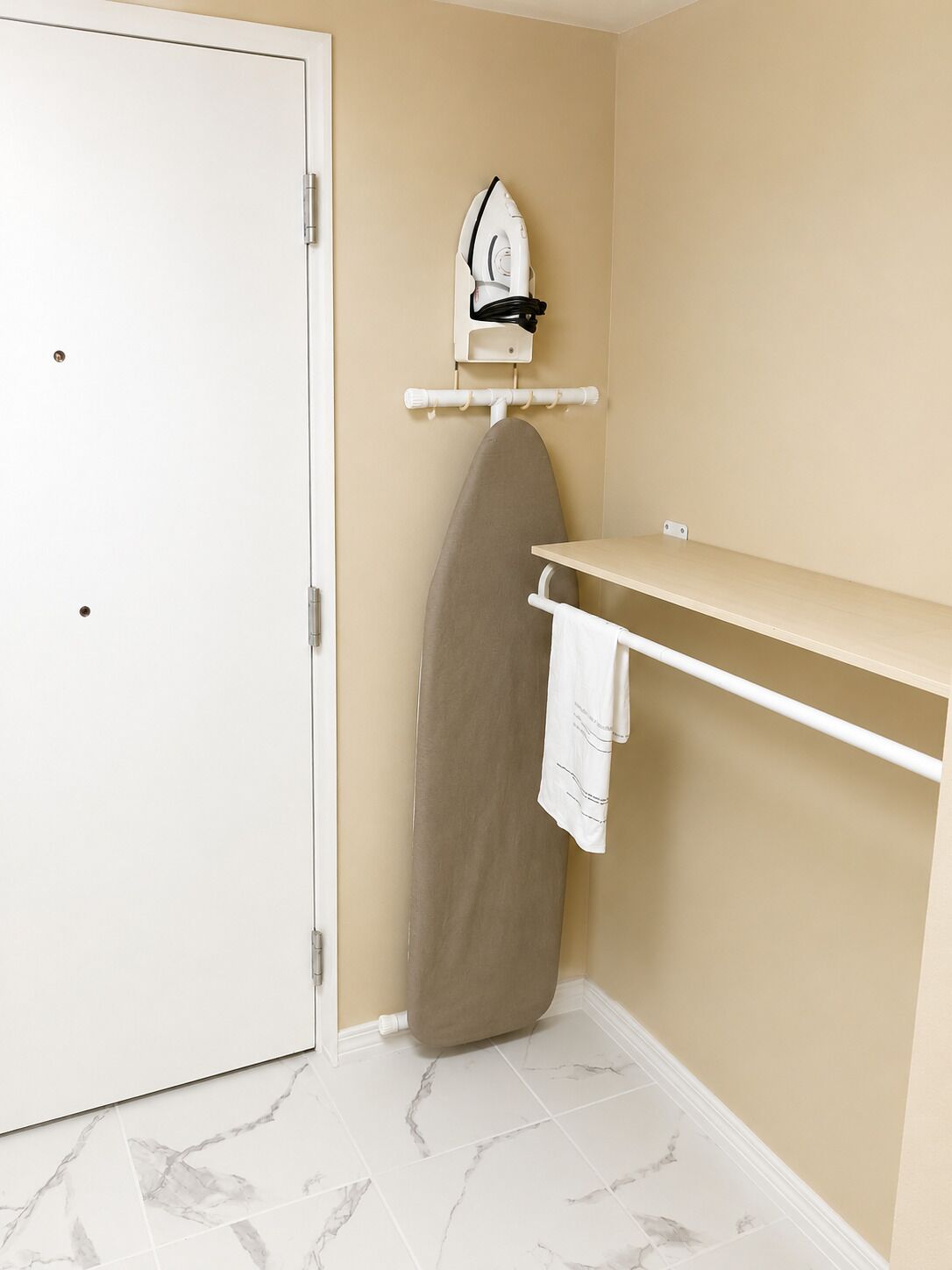 Baño con puerta blanca, tabla de planchar y toallero.