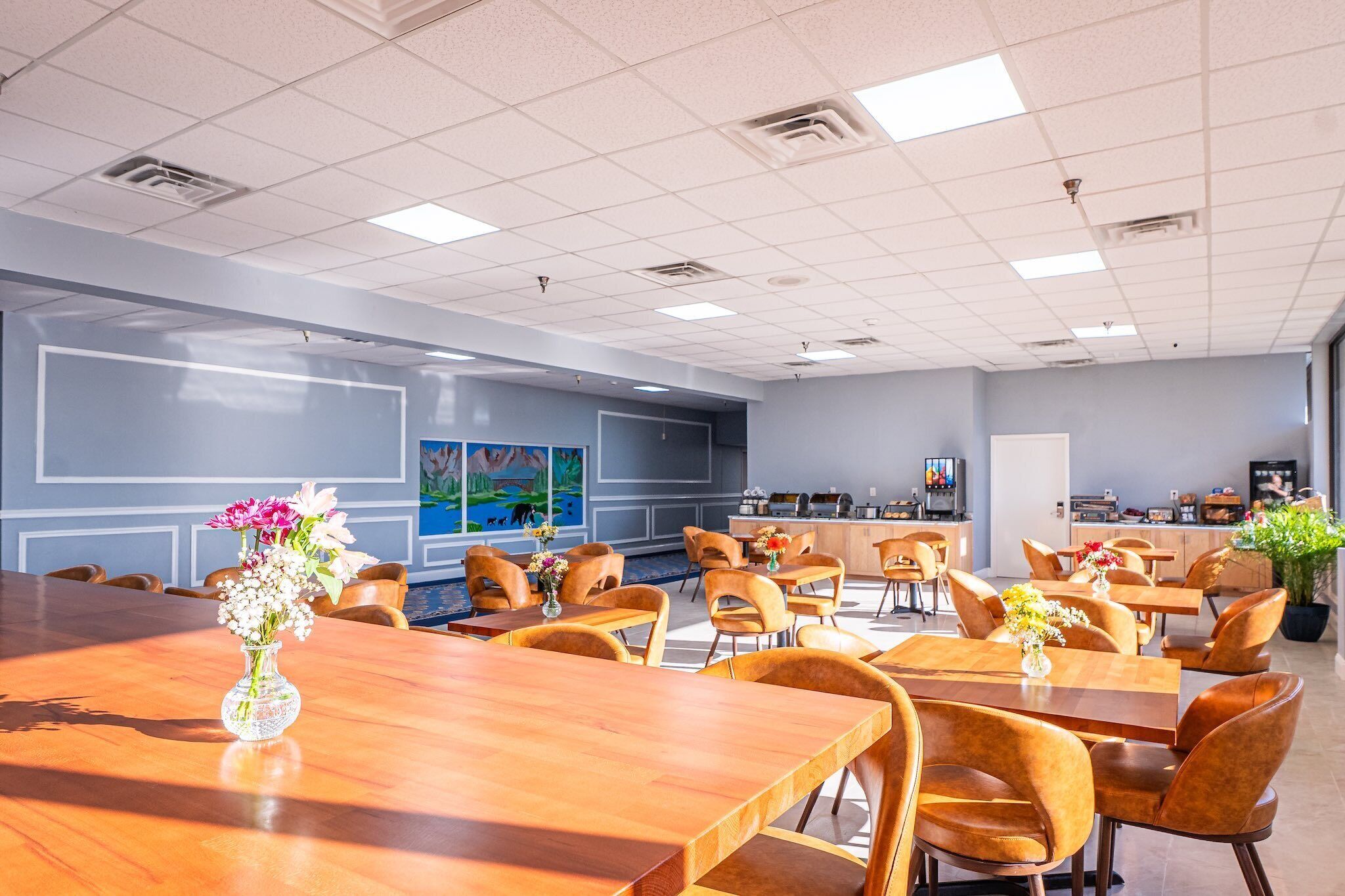 A conference room with multiple tables and chairs, a coffee station, and a large window with a view.