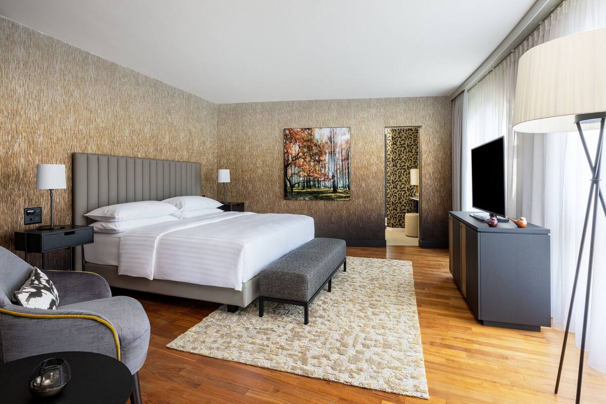 A modern hotel room with a large bed, a sofa, a TV, and a desk.