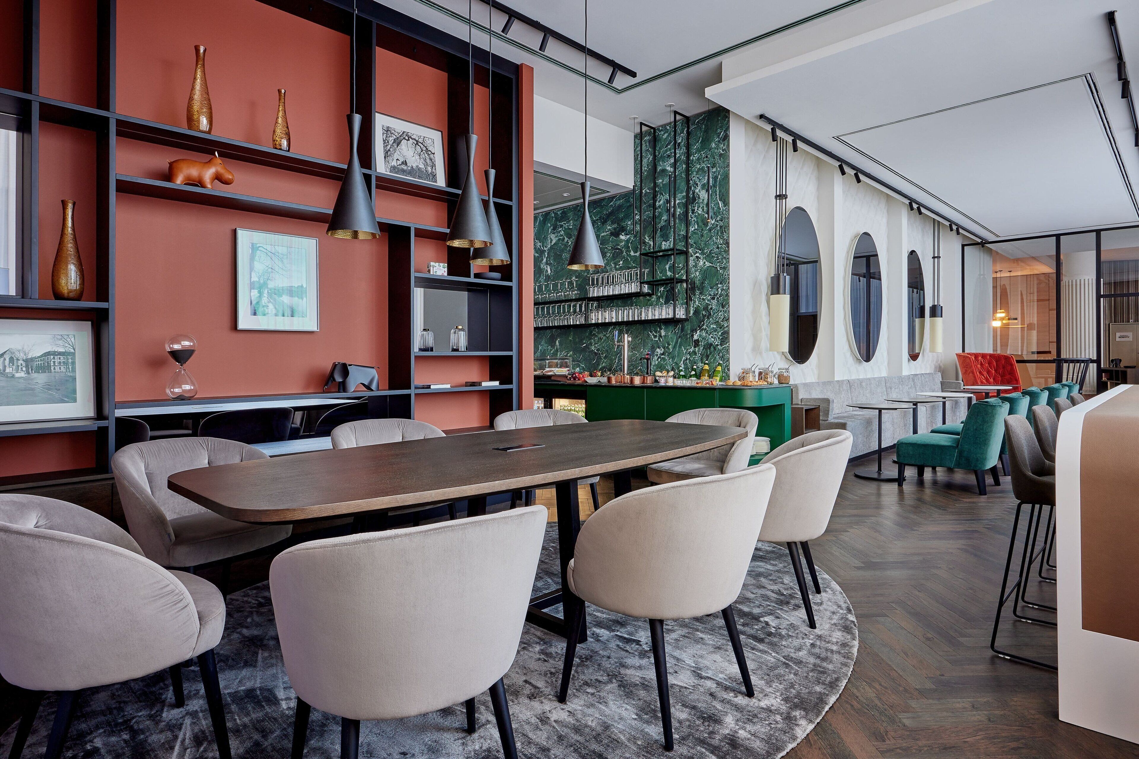 A modern interior with a long dining table, comfortable chairs, and a bar area with green seating.