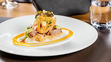 A white plate with a gourmet dish, a glass of water, and a dark-colored napkin on a wooden table.