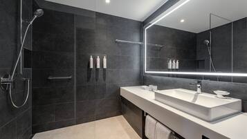 A modern bathroom with a large mirror, a walk-in shower, and a white sink.