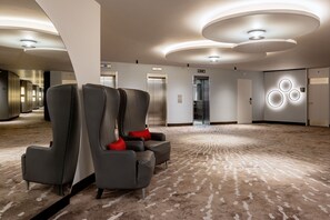 A spacious lobby with a carpeted floor, two grey armchairs with red cushions, and a modern ceiling design.