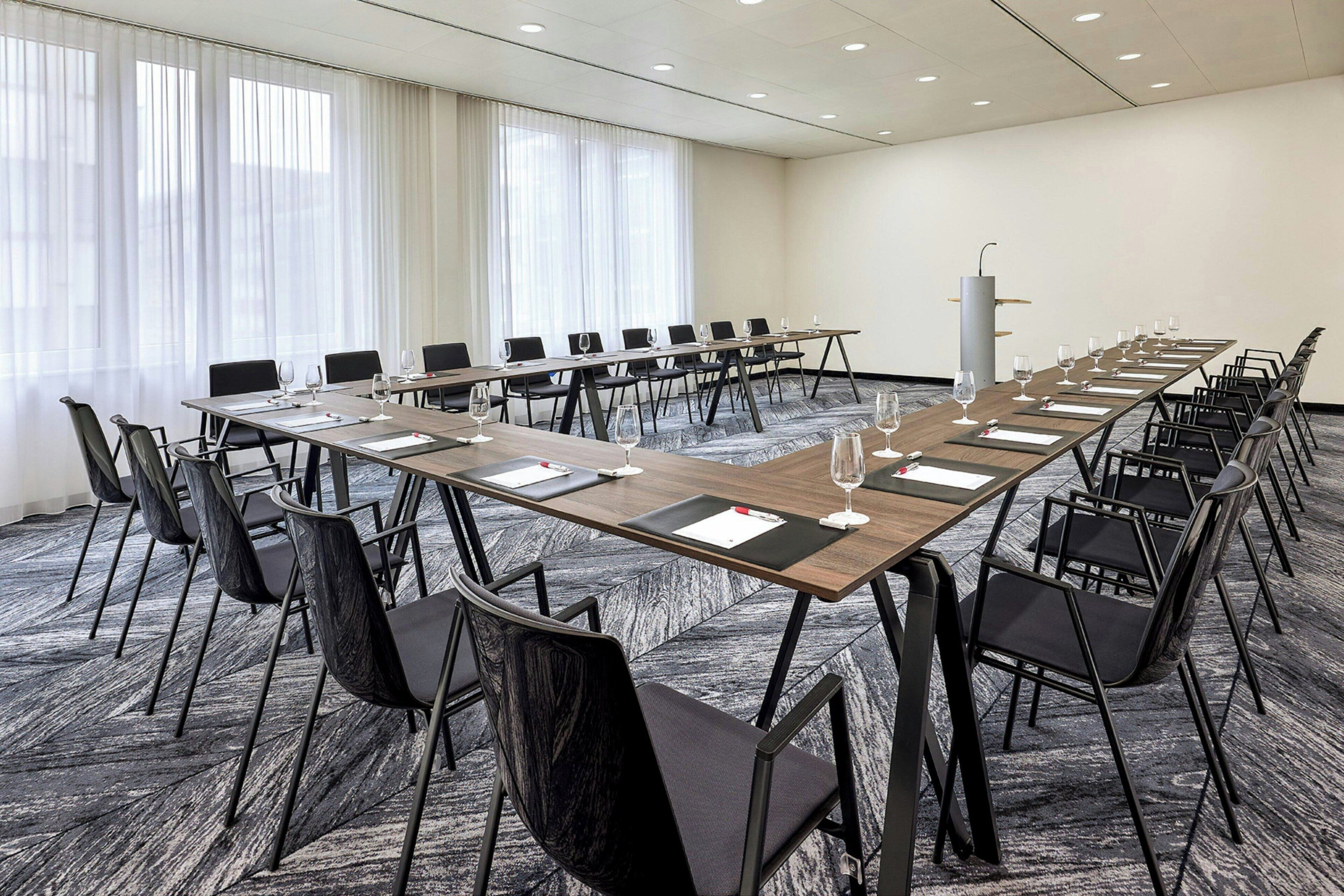 Una sala de conferències amb una taula llarga, cadiretes negres i un terraple d'alfabres.