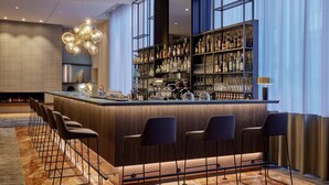 Zona de bar moderna con barra central, diversas opciones de asientos y una amplia selección de licores.