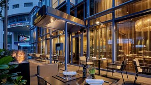Un área de comedor al aire libre con mesas y sillas, una chimenea y vistas del edificio del Centro de Convenciones al fondo.