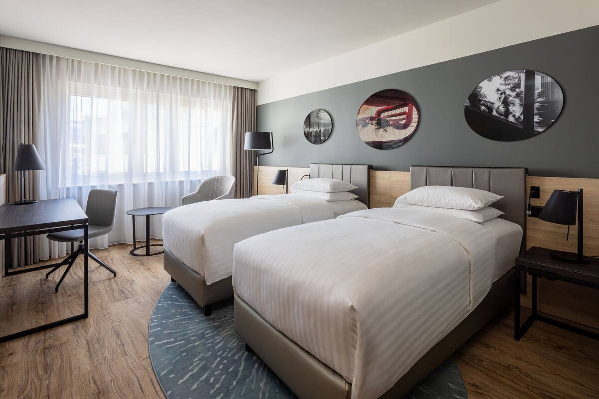 A hotel room with two beds, a desk, a chair, and a small table.