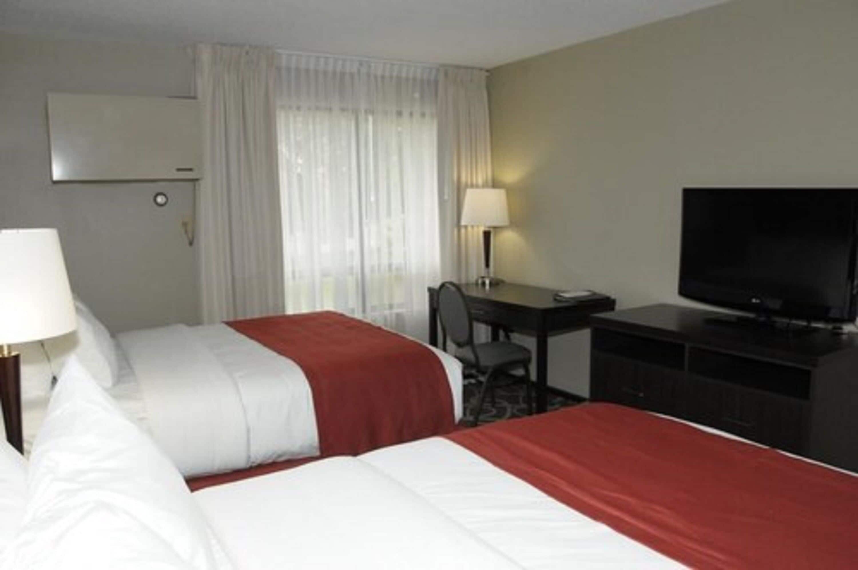 Une chambre d’hôtel avec deux lits, un bureau, une chaise, une télévision et une fenêtre avec des rideaux.