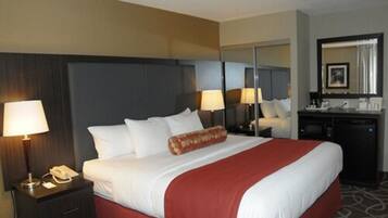 A hotel room with a large bed, a bedside table with a lamp, a mirror, and a small desk with a chair.
