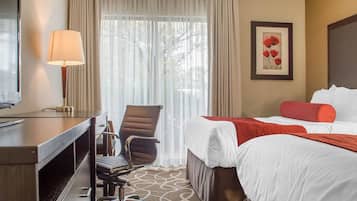 A hotel room with a bed, a desk, a chair, a TV, and a window with curtains.