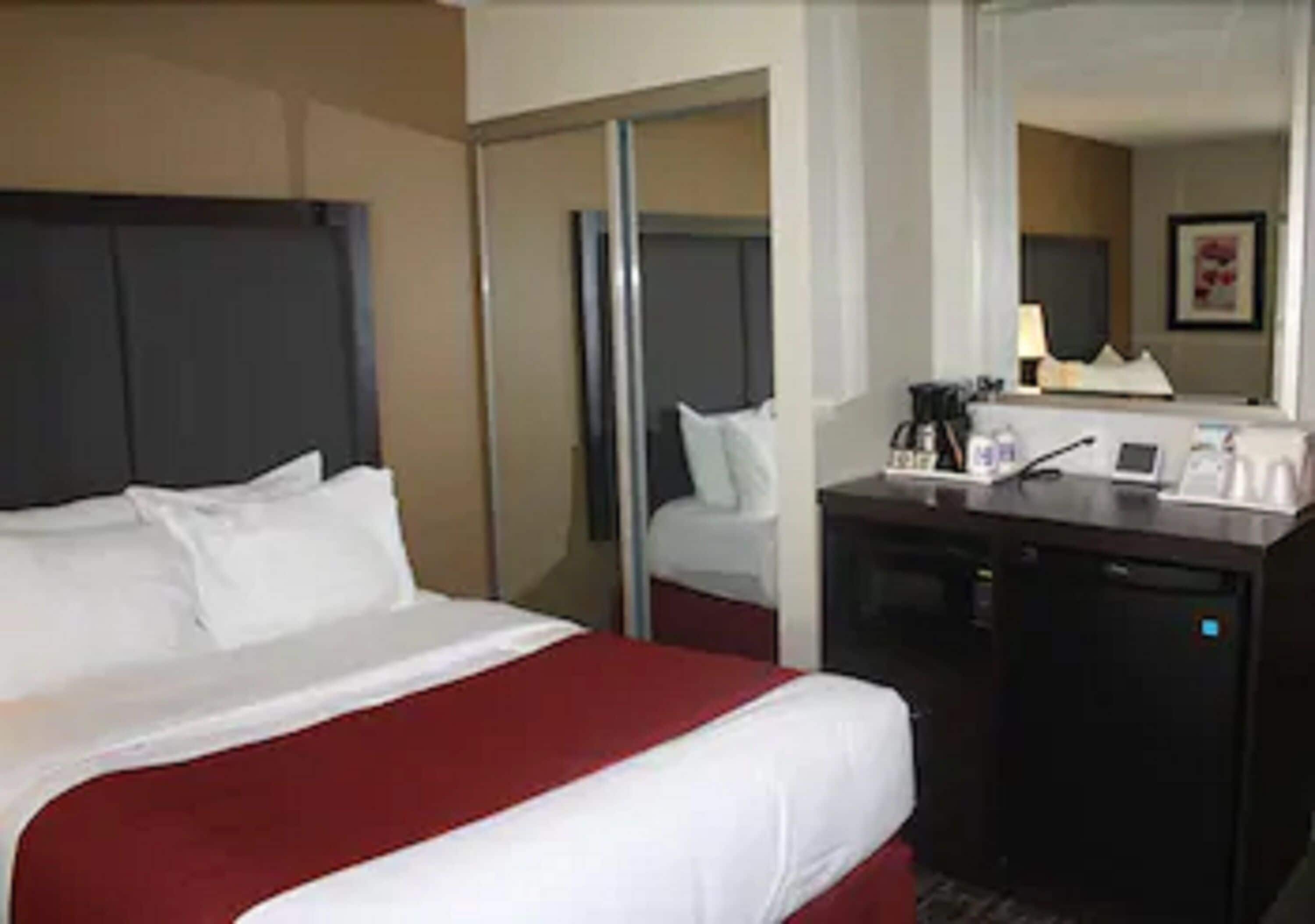 A hotel room with a bed, a desk, and a mirror.