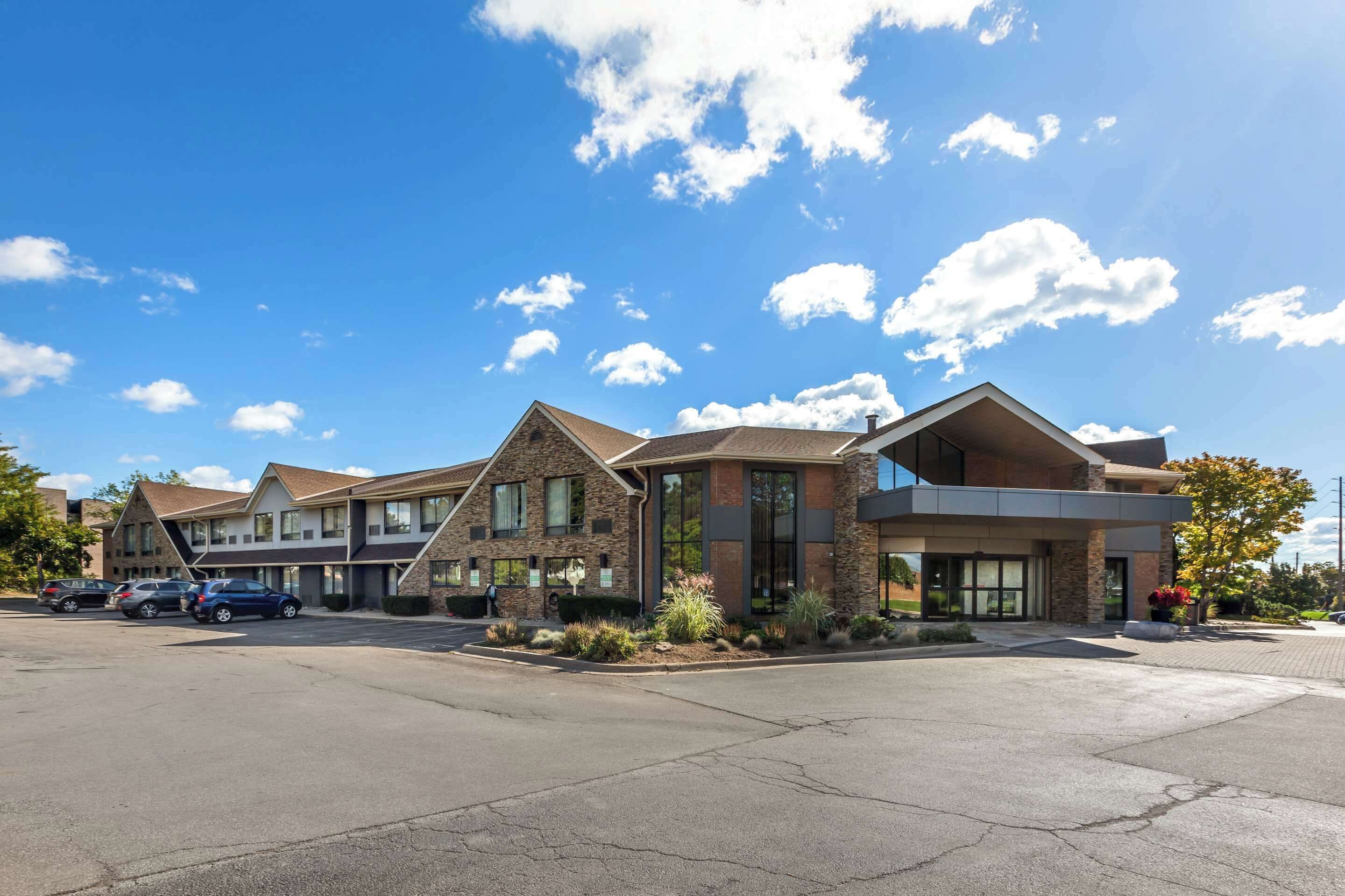 A hotel with a modern architectural design, featuring a mix of stone and glass facades, and a parking lot with several cars.