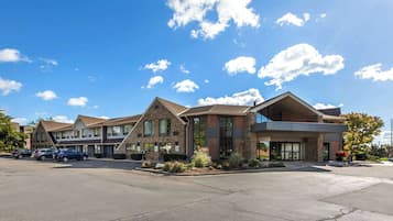 A hotel with a modern architectural design, featuring a mix of stone and glass facades, and a parking lot with several cars.