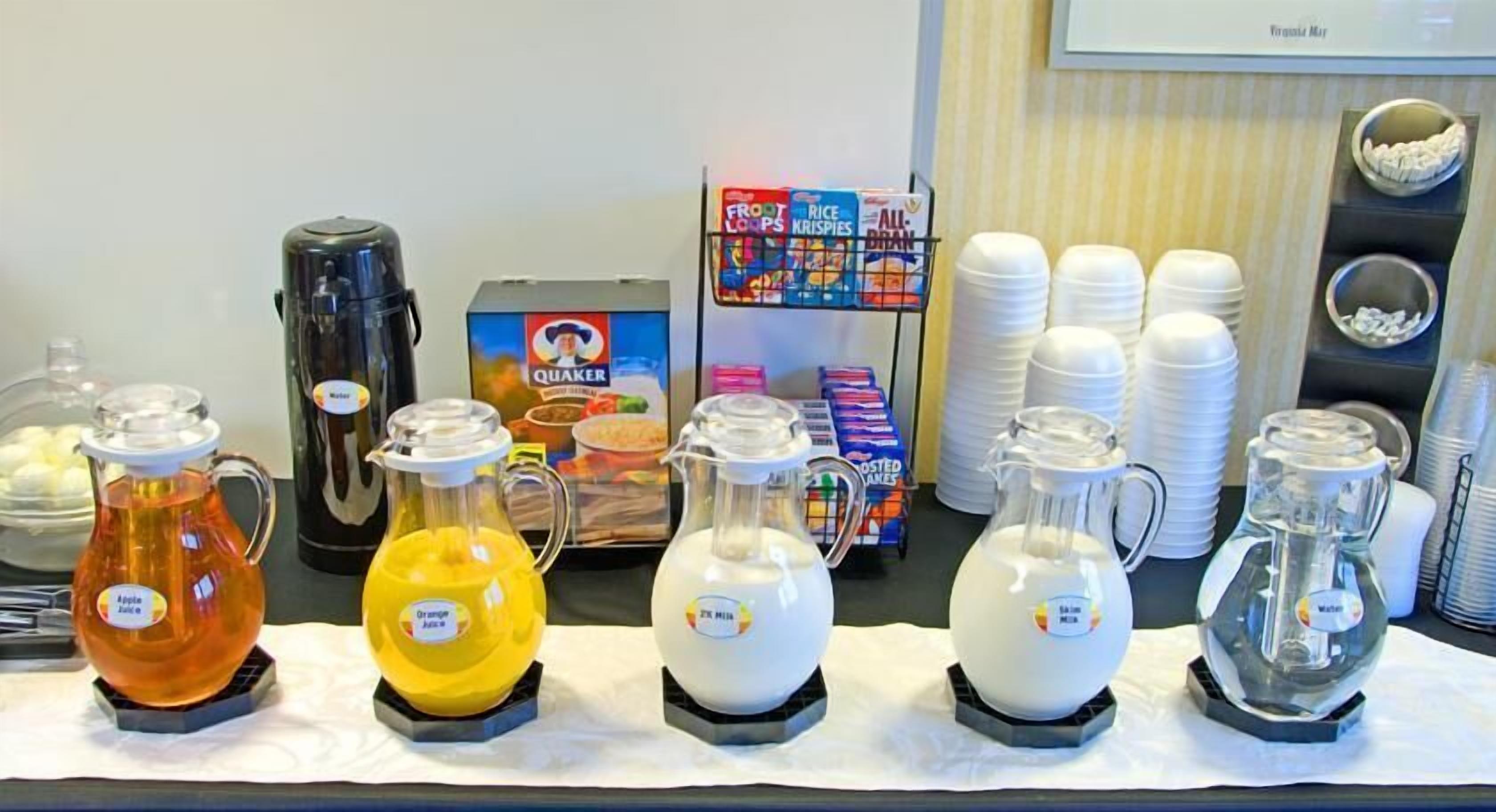 Un buffet de petit-déjeuner proposant une variété de boissons, notamment du jus de pomme, du jus d’orange et du lait, ainsi qu’une machine à café et des boîtes de céréales.