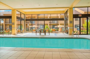 Piscina interior com espreguiçadeiras e guarda-sóis, rodeada por um edifício com várias varandas.
