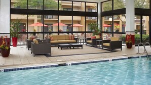 Un espace aménagé au bord de la piscine, avec des chaises longues et des parasols, une piscine et une vue sur un immeuble doté de balcons.