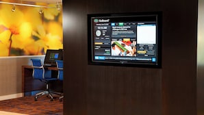 Un écran GoBoard dans le hall d’un hôtel, avec une fresque florale en arrière-plan, un comptoir d’accueil et un fauteuil de bureau bleu.