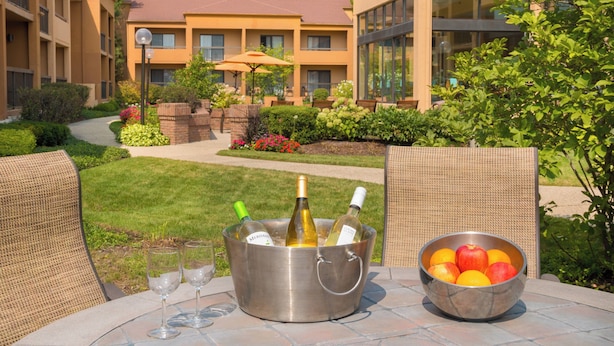 Une table placée au bord de la piscine, sur laquelle se trouve un seau en métal contenant des bouteilles de vin et des verres, ainsi qu’un saladier rempli de fruits.
