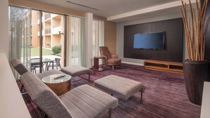 A modern living room with a flat-screen TV, comfortable seating, and a large window overlooking a courtyard. - Courtyard Fairfax Fair Oaks (Fairfax)