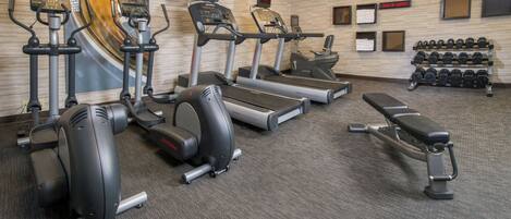 A gym with treadmills, elliptical machines, and a bench.
