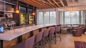 A bar area with a long counter, multiple stools, and a seating area with sofas and a round table. - Courtyard Fairfax Fair Oaks (Fairfax)