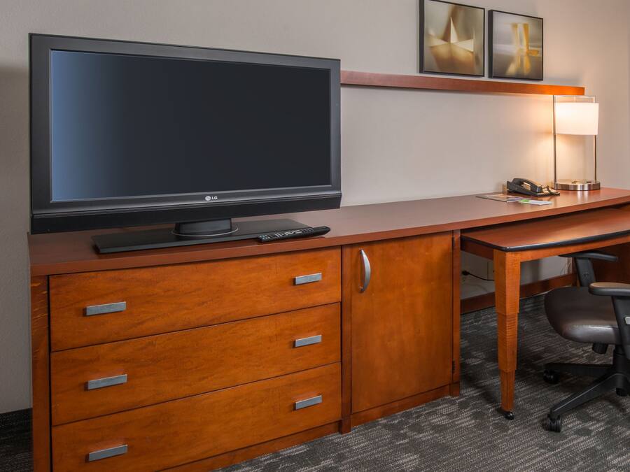 A hotel room with a wooden desk, a flat-screen TV, a lamp, and a chair.