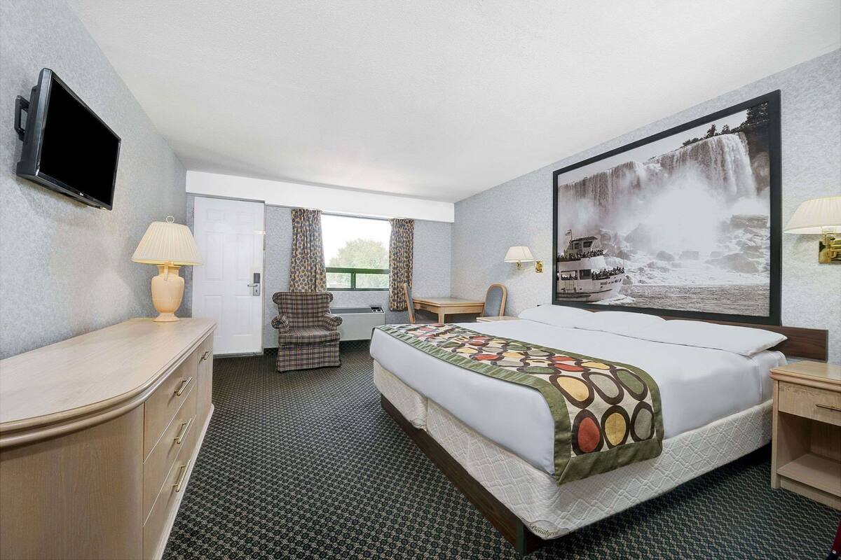 A hotel room with a bed, a desk, a chair, a TV, and a large window.