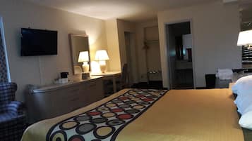 A hotel room with a bed, a desk with a lamp, a dresser, a television, and a bathroom visible through an open door.