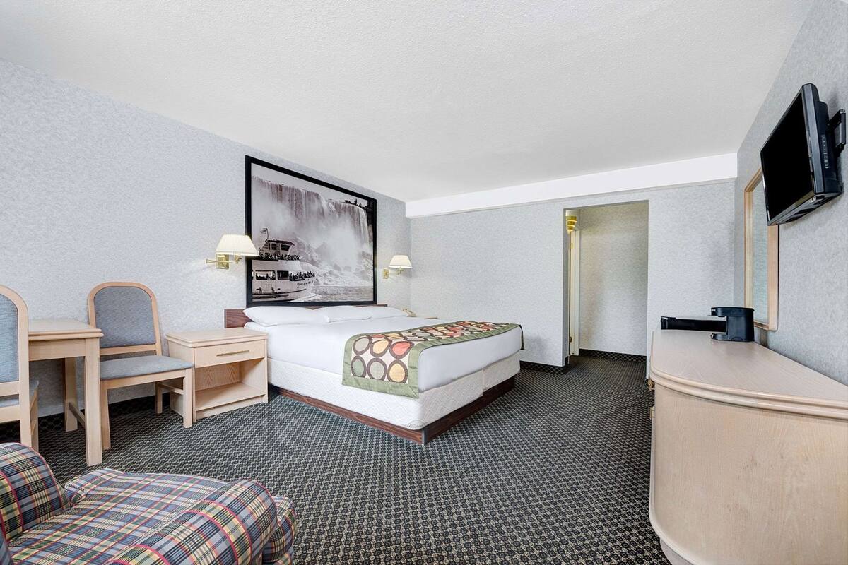 A hotel room with a bed, a desk with a chair, a television, and a large framed picture on the wall.