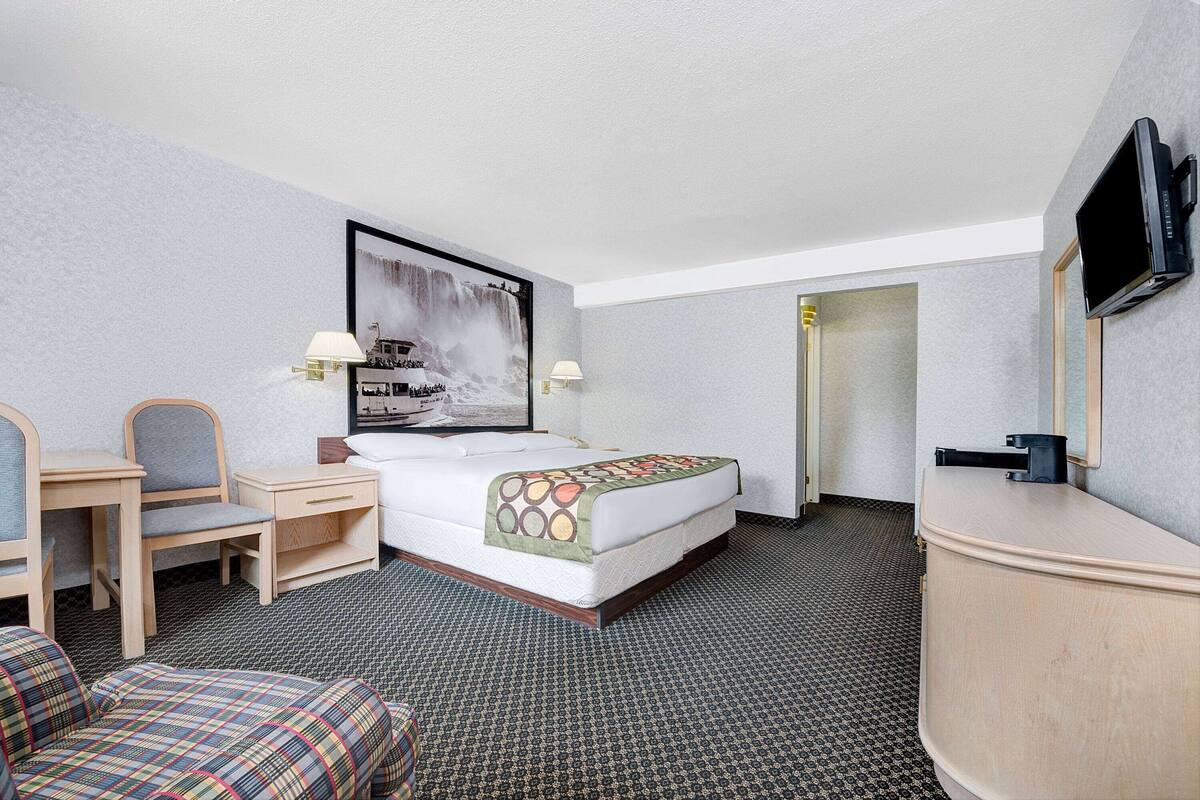 A hotel room with a bed, a desk, a chair, a television, and a bathroom door.
