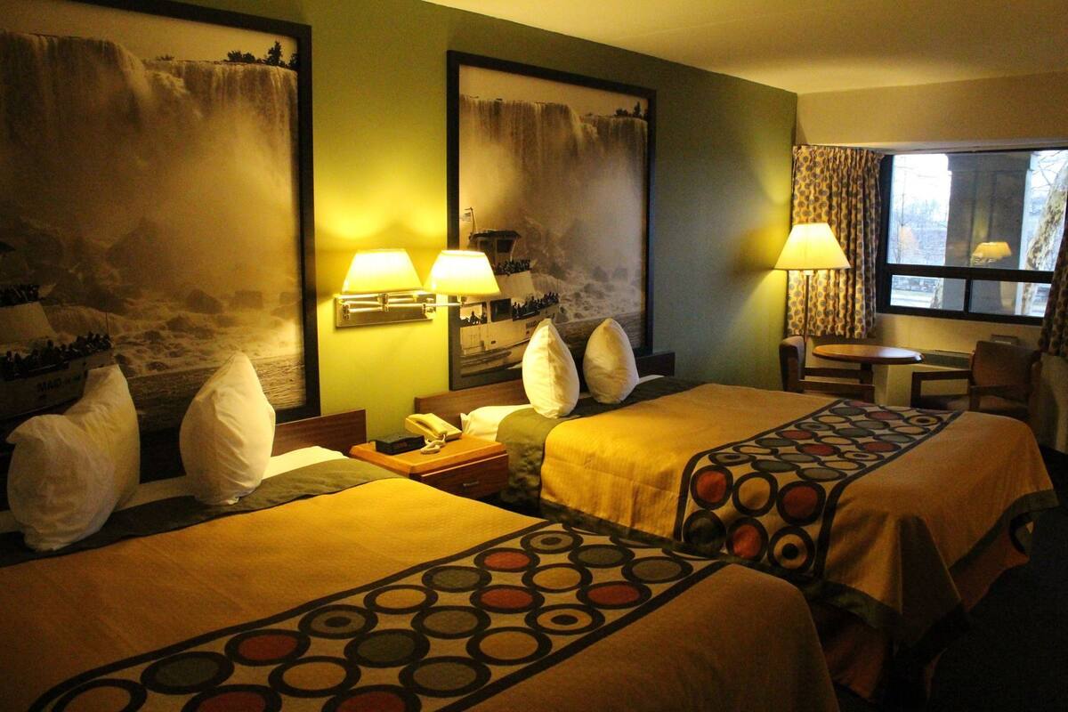 A hotel room with two beds, a desk, a chair, and a window with curtains.