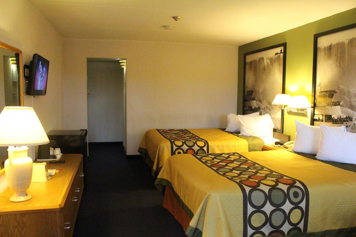 A hotel room with two beds, a desk with a lamp, a television, and artwork on the walls.
