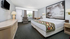 Una habitación de hotel con cama, escritorio, silla, televisión y un ventanal grande.