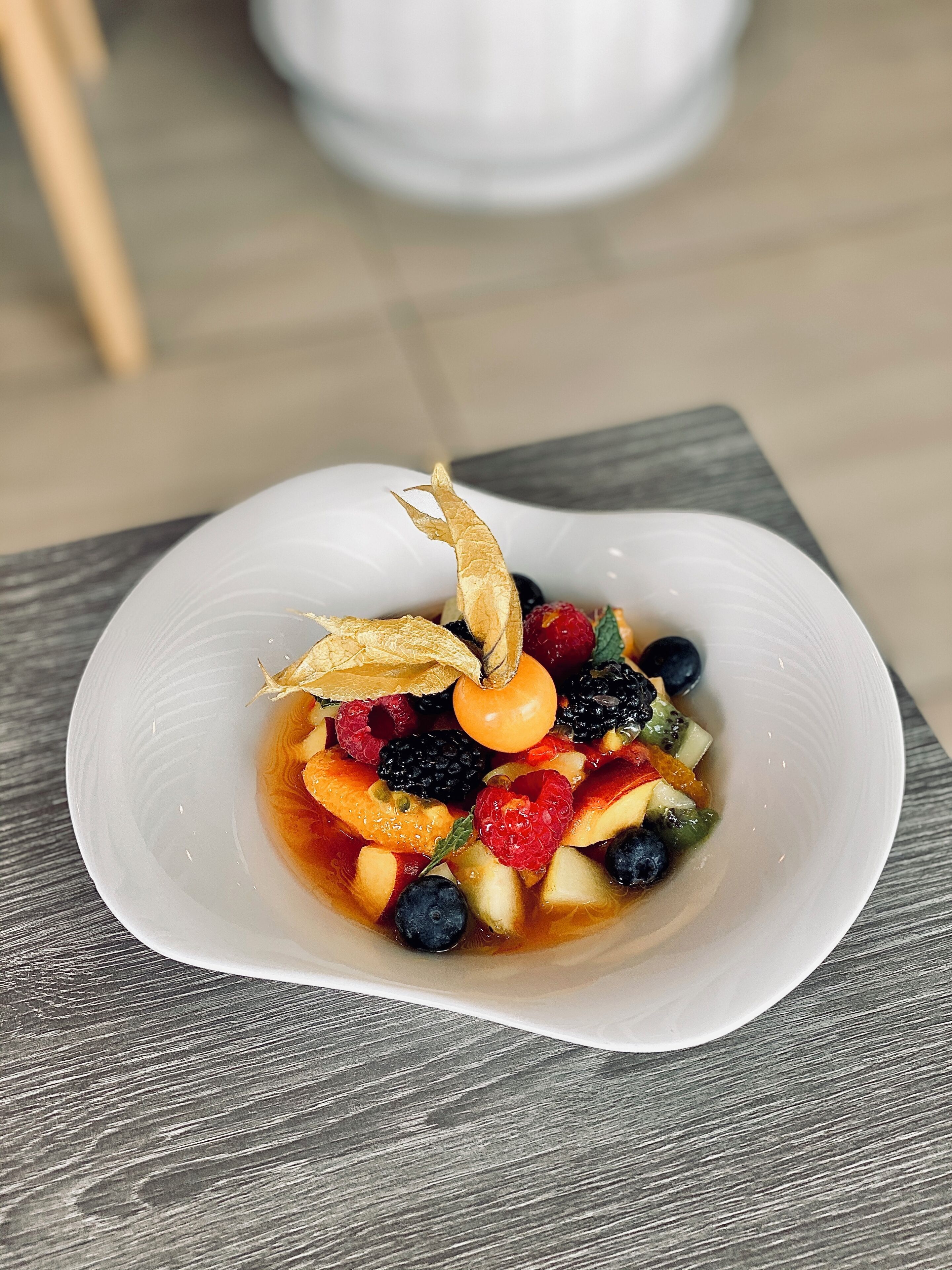A white bowl of fruit salad on a wooden table.