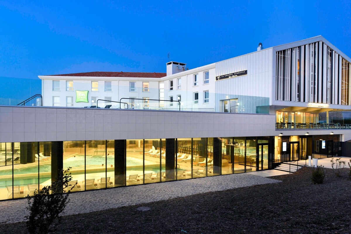 A modern hotel with a pool area, a terrace, and a dining area.