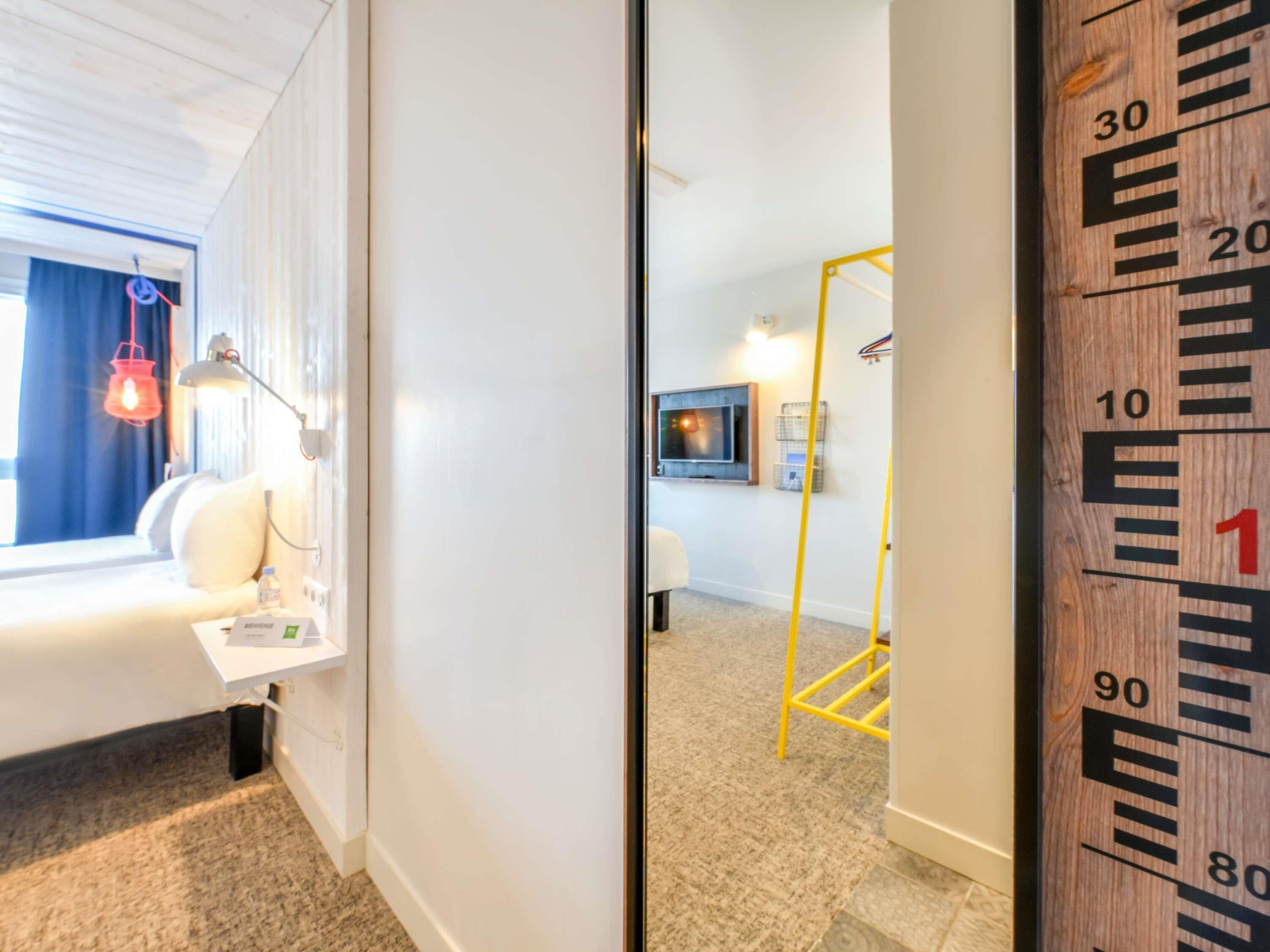 A hotel room with a bed, bedside table, lamp, and a window with curtains.