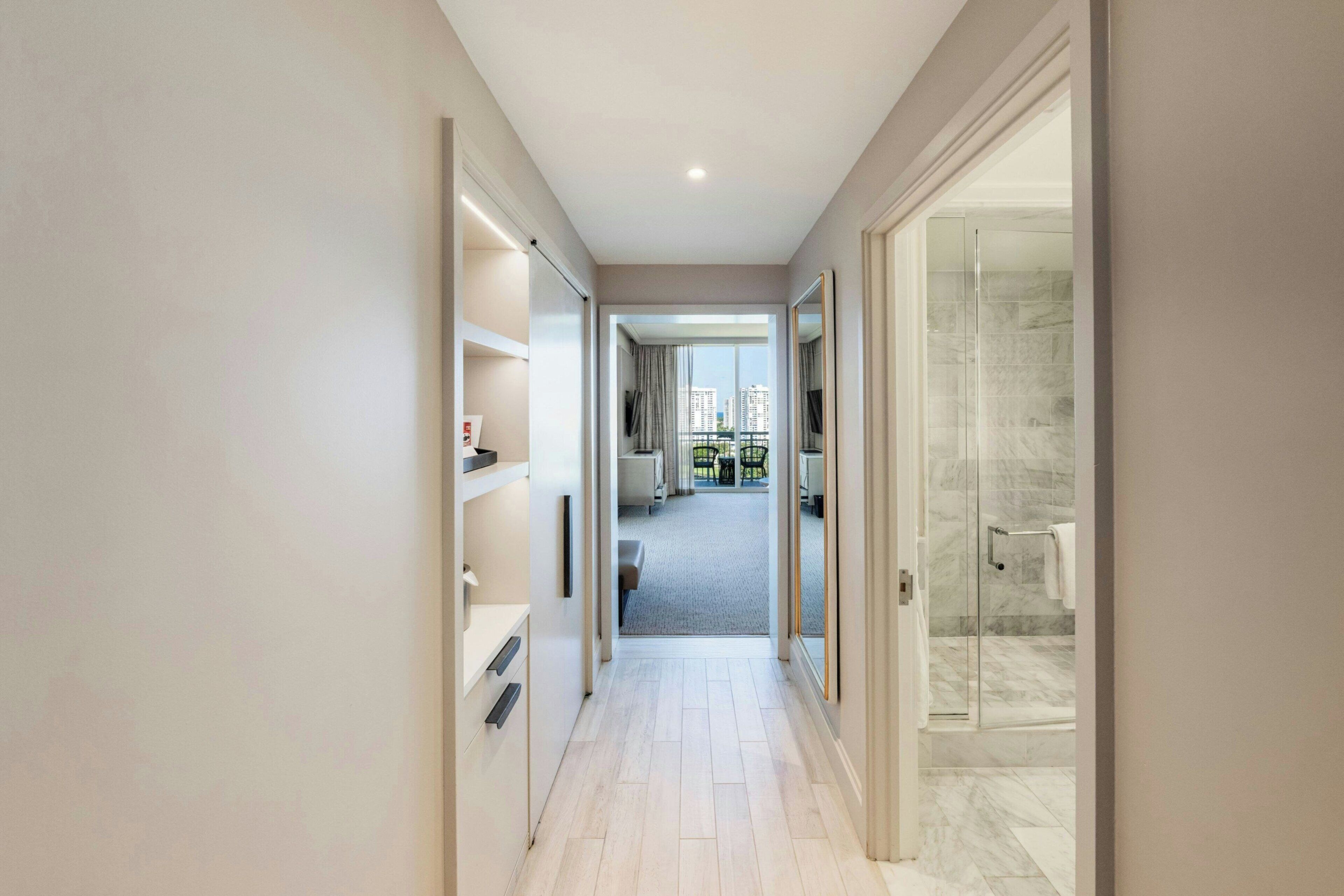 Un pasillo que conduce a un baño con mampara de vidrio y vistas a la ciudad.