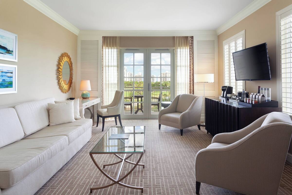 A modern living room with a sofa, armchairs, a glass coffee table, and a television.