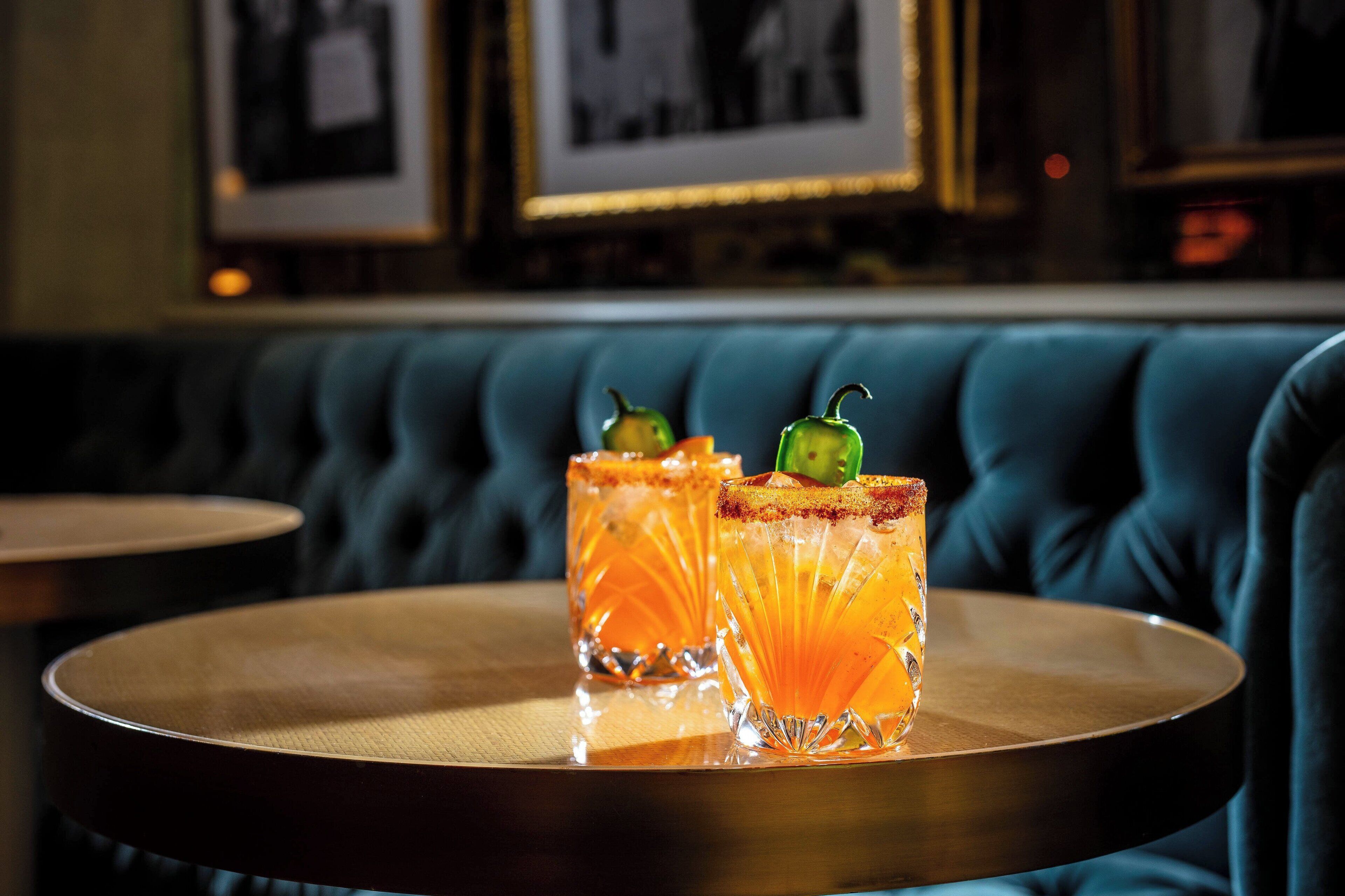 Two cocktails on a round wooden tray on a blue upholstered sofa.