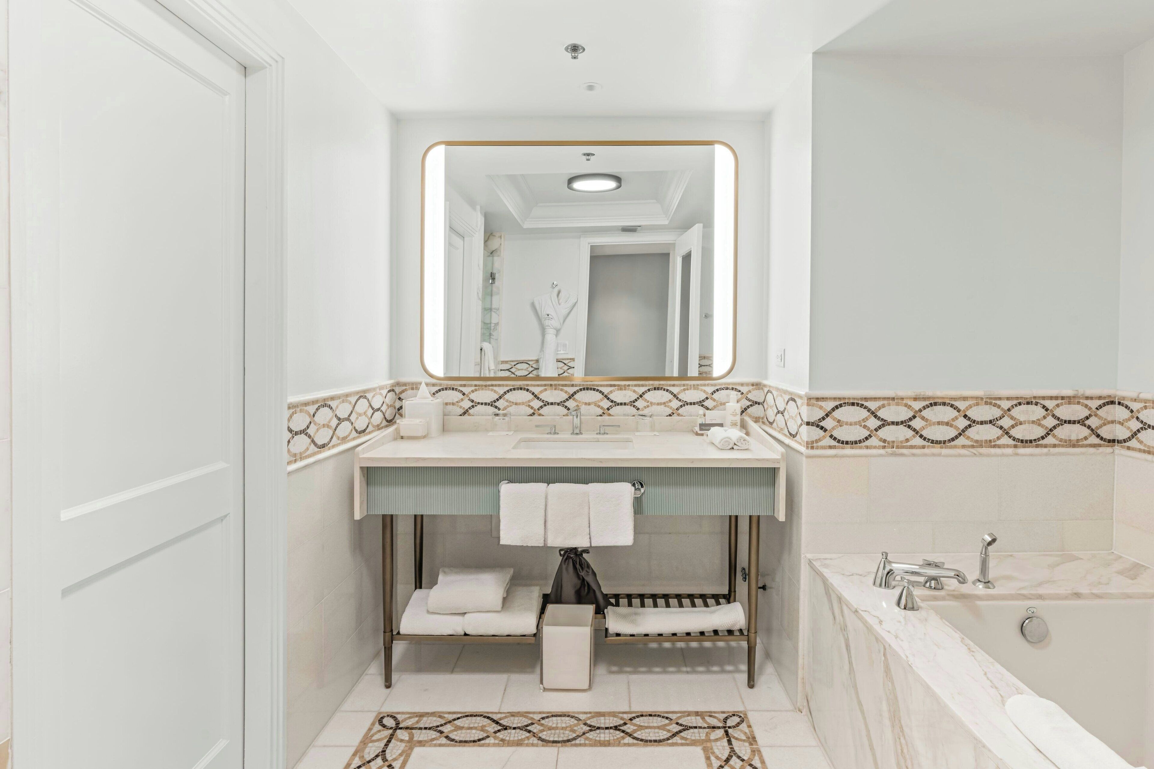 A modern bathroom with a large mirror, a sink with a towel rack, a bathtub, and a vanity with a towel warmer.