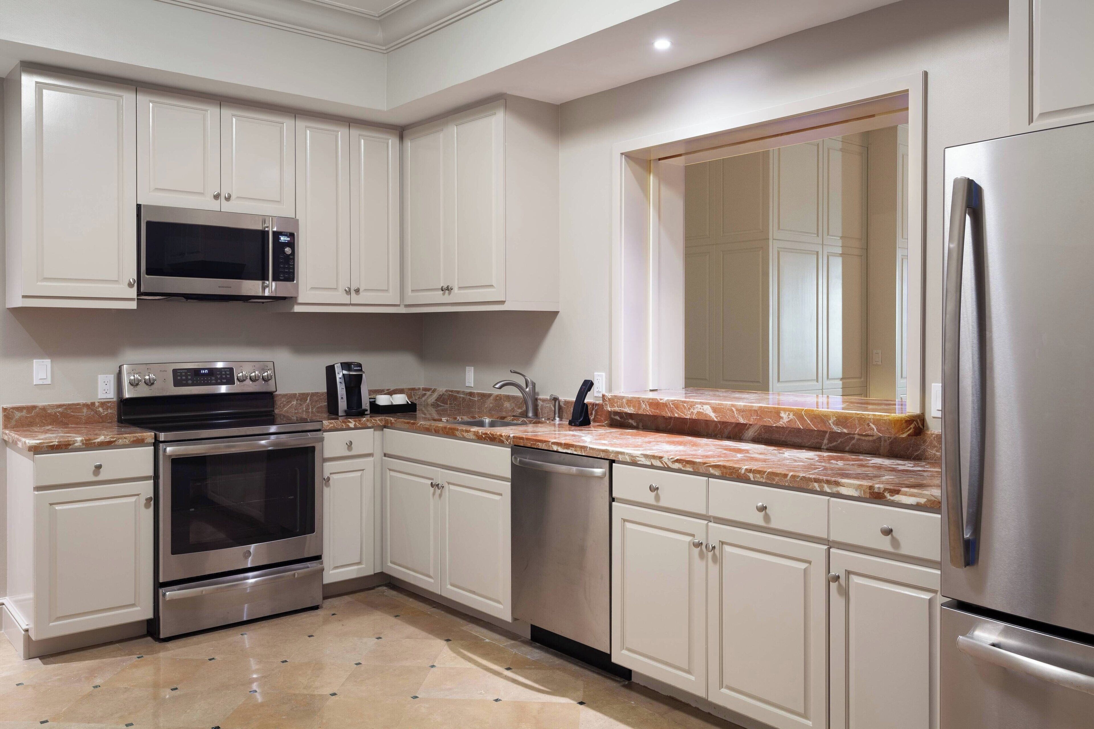 A modern kitchen with stainless steel appliances, white cabinetry, and a marble countertop.