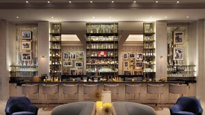 A bar area with multiple shelves of bottles and glasses, bar stools, and framed pictures on the walls.
