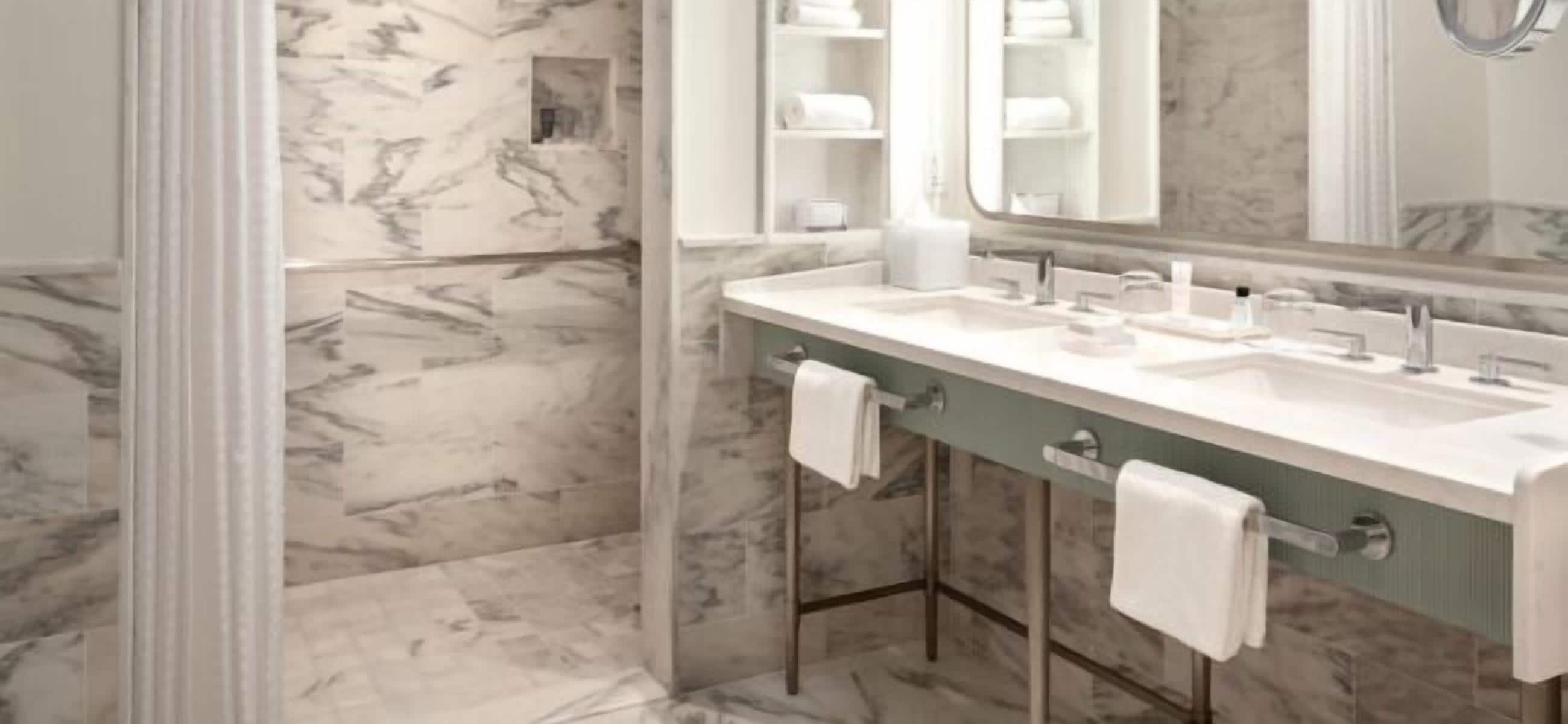 A bathroom with marble walls, a double sink vanity, and a large mirror.