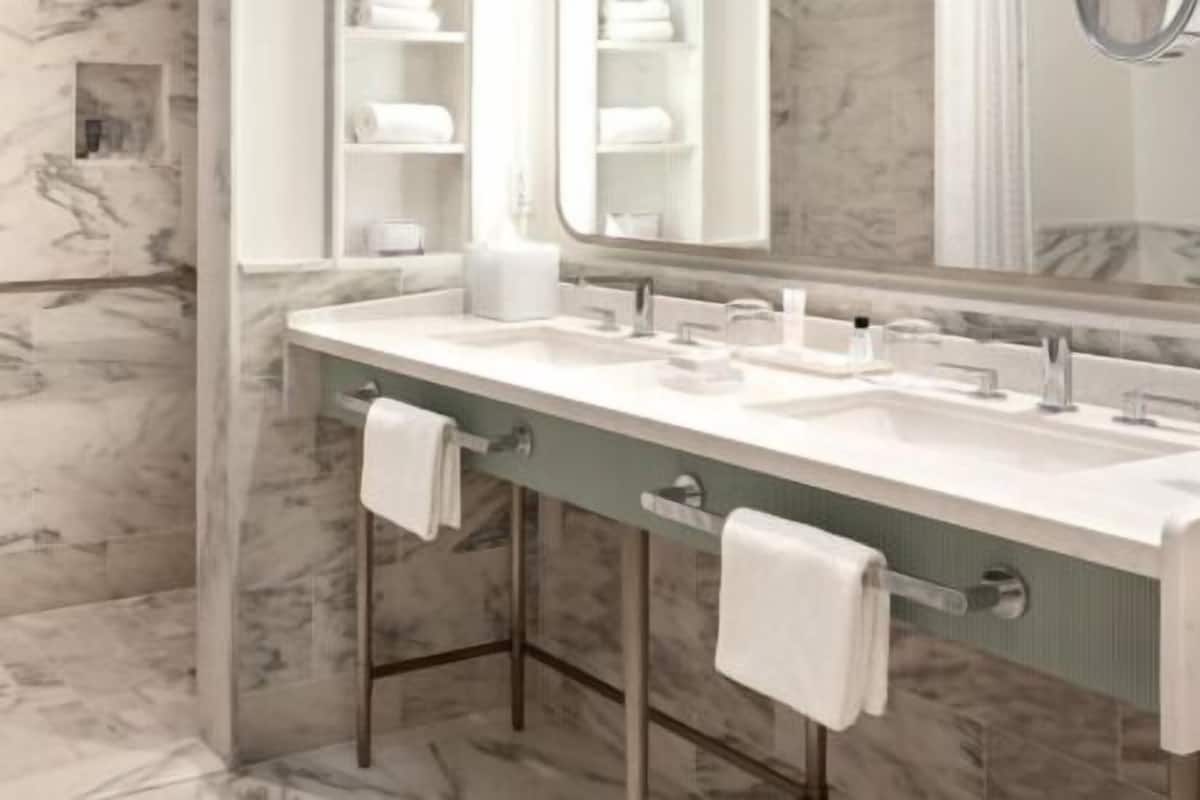 A bathroom with marble walls, a double sink vanity, and a large mirror.