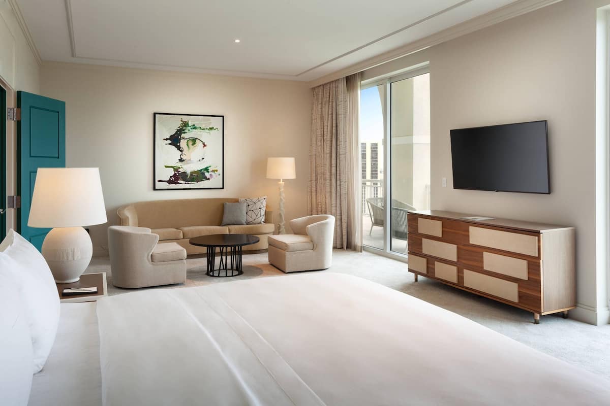 Una habitación de hotel con una cama grande, un sofá, una mesa de centro, un televisor y vistas a la ciudad a través de la ventana.