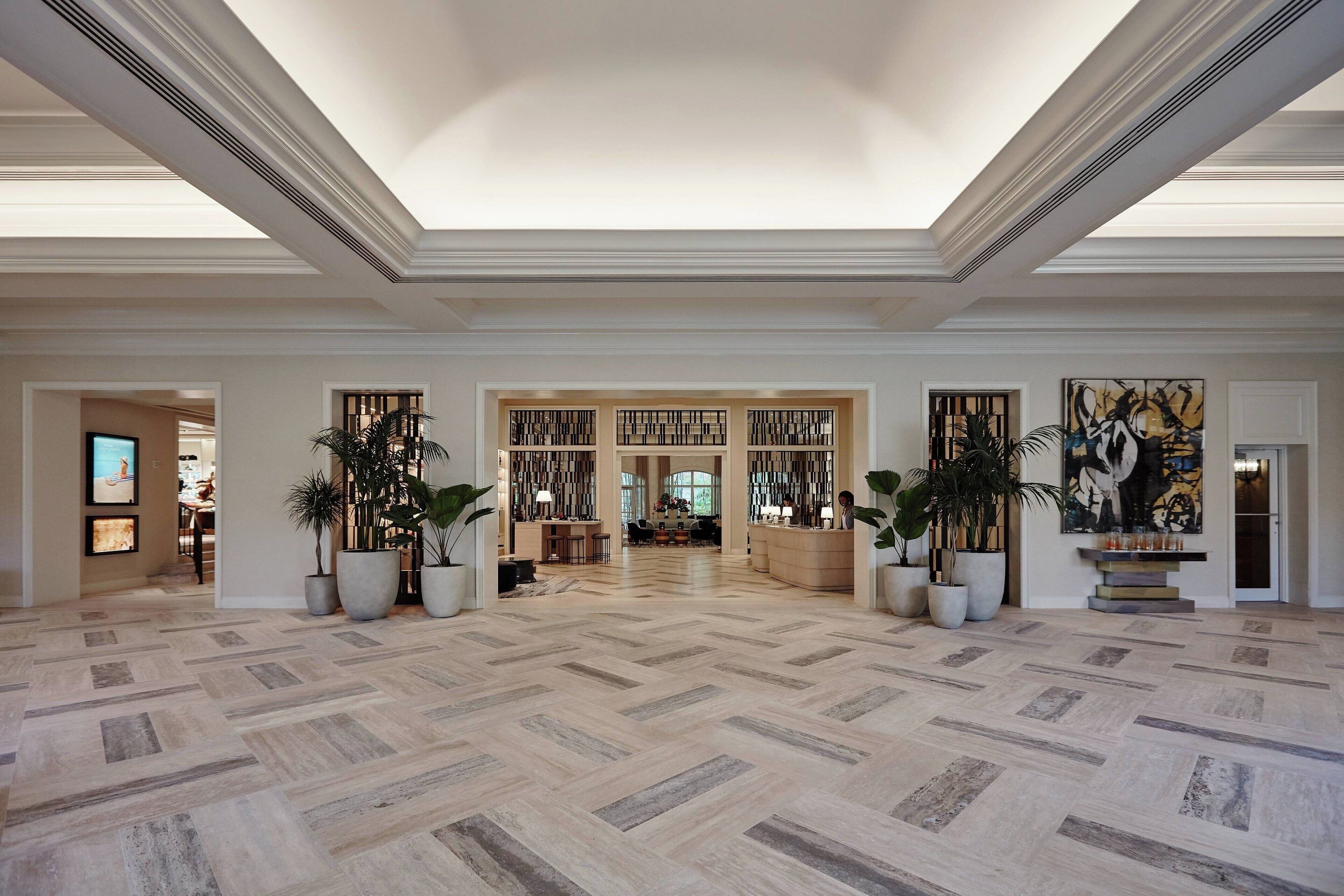 Eine geräumige Lobby mit Fischgrätparkett, großen Kübelpflanzen, einem Empfangsschalter und einem großen abstrakten Gemälde an der Wand.